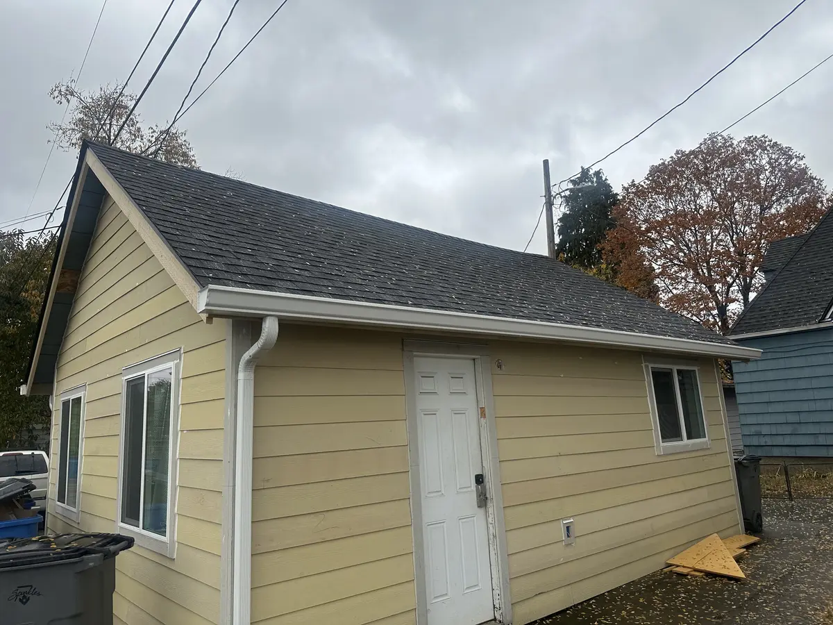 Single-story gabled home in Vancouver, WA with a dark gray shingle roof, new white seamless gutters and downspout, new fascia boards and bargeboards, and tan lap siding
