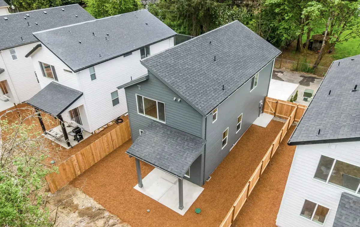 Aerial view of newly built two-story cottages in Vancouver, WA with new charcoal-gray shingle roofs, a gray-sided cottage with a shingled covered patio, and fenced backyards