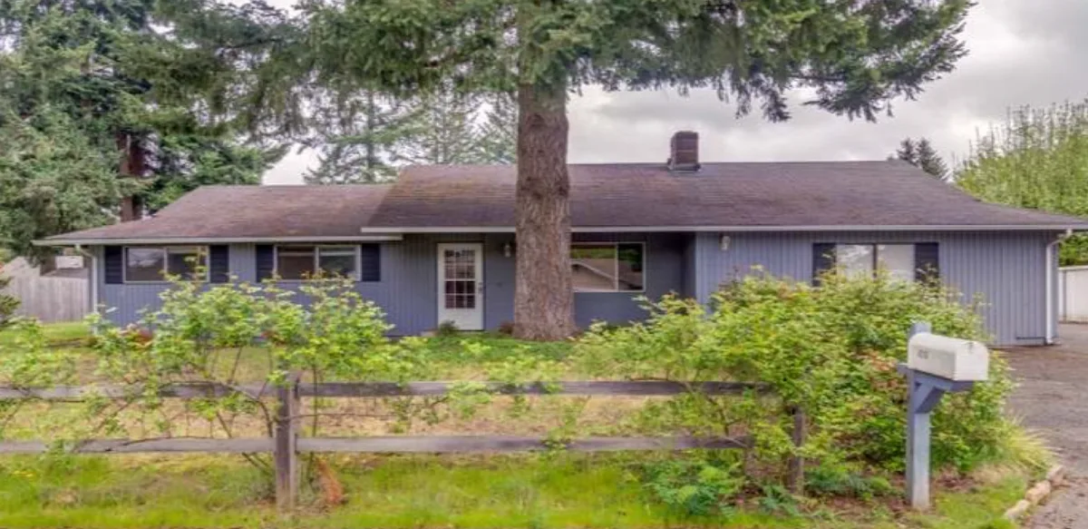 The same ranch home before, with a weathered, faded roof and blue vertical siding