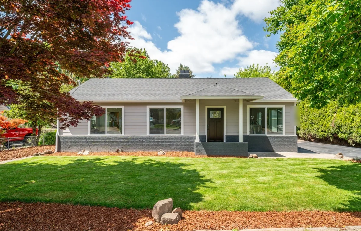 Single-story ranch home in Tigard, OR with a new gray shingle roof, a gabled front porch, light gray siding, and a painted brick base