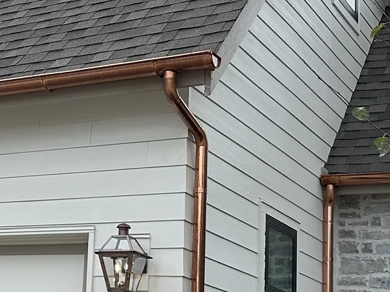Copper seamless gutter and downspout on a home with light gray siding